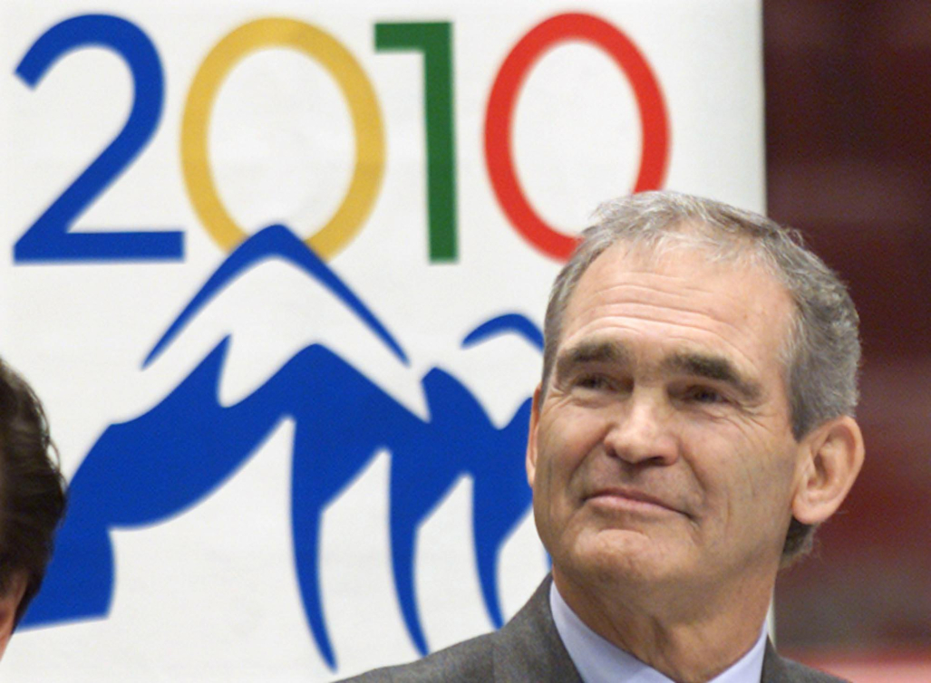 Jack Poole pose devant le logo des Jeux de Vancouver 2010